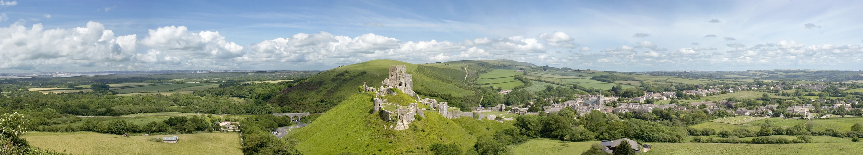 Wide summer panorama of Corfe Castle and the village in the valley below